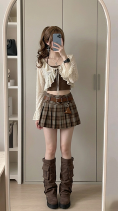 Person in a plaid skirt, crop top, and brown boots taking a mirror selfie