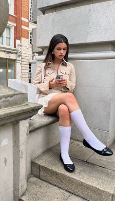 Woman with long hair sitting on a stone ledge on a street, looking at her phone