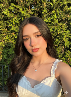 Woman with long dark hair wearing a white top and necklace outdoors