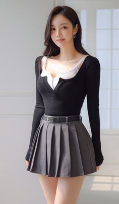 Woman with long dark hair wearing a black top and gray pleated skirt indoors