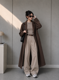 Woman in a long brown coat and wide leg pants posing indoors