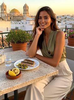 Woman smiling at a rooftop restaurant with a cityscape view at golden hour