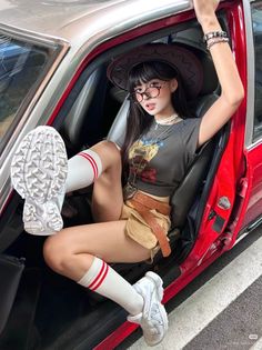 Woman in a cowboy hat and crop top sitting in a red car with one leg out