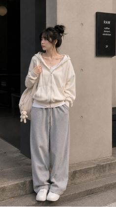 Woman in a cream hoodie and grey sweatpants with a bun hairstyle outdoors