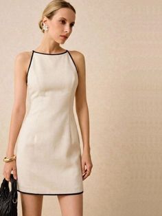 Woman in a cream mini dress with black trim, holding a black bag