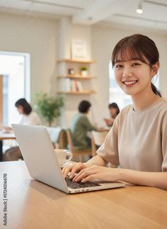 Woman smiling while typing on a laptop in a bright cafe