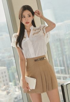 Woman in a white blouse and pleated skirt holding a handbag indoors