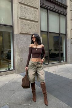 Woman in an off-shoulder top and denim shorts with knee-high boots on a city street