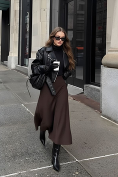 Woman in a black leather jacket and brown midi skirt walking on a city street