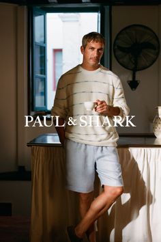 Man in a striped sweater and light blue shorts holding a cup indoors