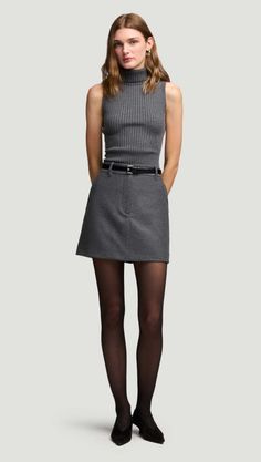 Woman in a gray ribbed turtleneck top and mini skirt with black tights