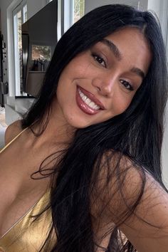 Woman with long black hair and freckles smiling in a gold top indoors