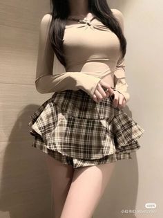 Woman with long hair wearing a plaid skirt and cropped top indoors