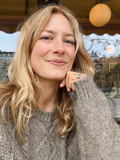 Woman with blonde hair wearing a cable knit sweater and an emerald ring