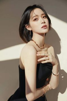Woman with short black hair wearing a black dress and jewelry, with dramatic lighting