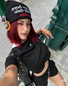 Person with red hair wearing a beanie, headphones, crop top, and shorts outdoors