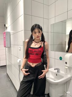 Woman with pigtails in a red crop top and black pants in a bathroom