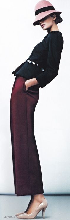 Woman in a pink hat, black jacket, and burgundy pants posing in a studio