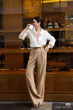 Woman in a white shirt and wide leg pants holding a cup indoors