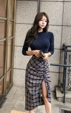 Woman with long hair wearing a long sleeve top and plaid skirt with a high slit
