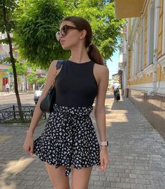 Woman in a black top and floral skirt walking on a sunny street