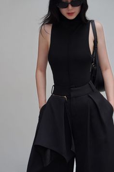 Woman in a black turtleneck top and wide-leg pants with sunglasses and a shoulder bag