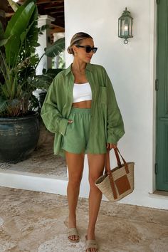 Woman in a green shirt and shorts with a white crop top and straw bag