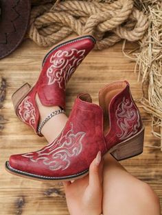 Red cowboy boots with white embroidered designs on a wooden background