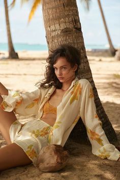 Woman with long wavy hair leaning against a palm tree on a beach