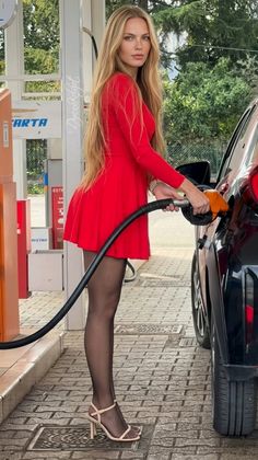 Woman in a red dress and pantyhose fueling a car at a gas station