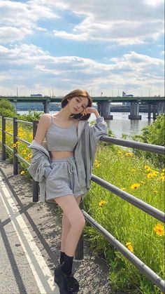 Woman in a grey crop top and shorts leaning on a railing by a river
