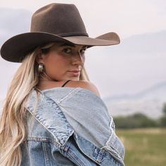 Woman in a cowboy hat and denim jacket looking over her shoulder outdoors