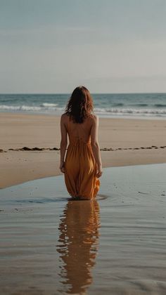 Woman in a long orange dress standing in shallow water on a beach