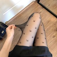 Person wearing black patterned tights and a short skirt, holding the tights