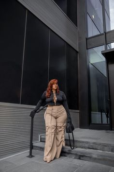 Woman with long red hair wearing a black crop top and cargo pants outdoors