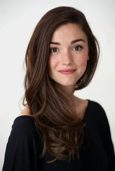 Woman with long brown hair and freckles wearing a black top against a white background