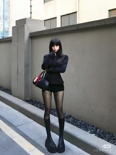 Woman with long black hair wearing a black top, shorts, and platform boots outdoors