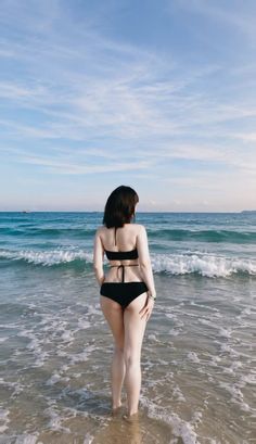 Woman in a black bikini standing in the ocean with her back to the camera