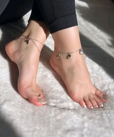 Feet with anklets and green nail polish on a white fluffy surface
