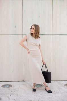 Woman in a beige midi dress and sunglasses holding a black handbag outdoors