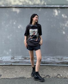 Woman with long black hair wearing a t-shirt, denim shorts, and combat boots outdoors