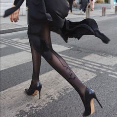 Person in a black dress and sheer tights with high heels walking on a street
