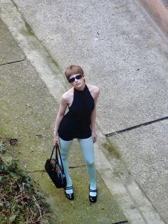 Woman with short hair and sunglasses wearing a black top and light blue tights