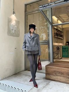 Woman in a grey jacket, pleated skirt, and beret standing outside a cafe