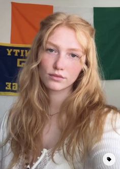 Woman with long blonde hair and freckles wearing a white top indoors