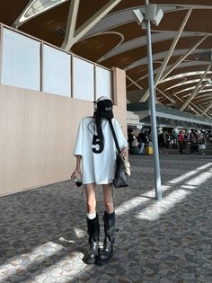 Person in an oversized white t-shirt and tall boots at an airport
