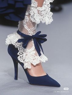 Close up of a foot in a navy blue high heel with white lace socks and a velvet ribbon