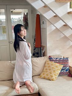 Woman in a white shirt dress kneeling on a sofa indoors