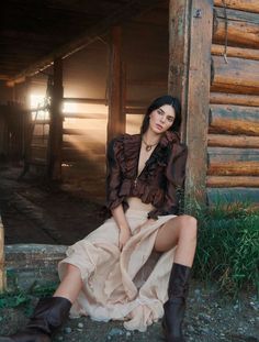 Woman in a ruffled blouse and long skirt sitting by a wooden cabin