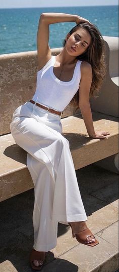 Woman in a white tank top and white pants sitting outdoors